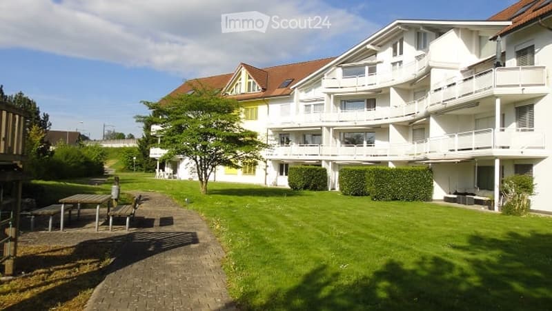 Apartment building with balconies, several floors, garden area, lawn, trees, pathway