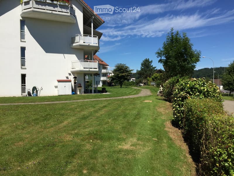 2 story building with red roof, balconies, green grass, streetlight, shrubs, walkway, bushes