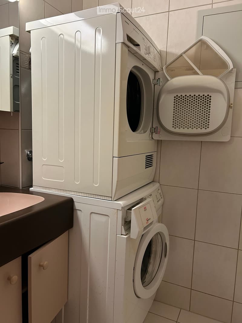 Bathroom with a stacked washing machine and dryer unit, a sink, and tiled walls.