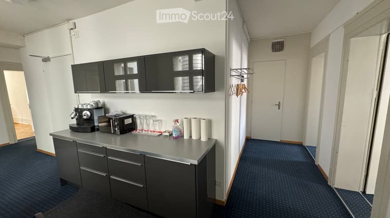 Break room with a grey countertop, black cabinets, coffee machine, microwave, cups, paper towels, and cleaning supplies.