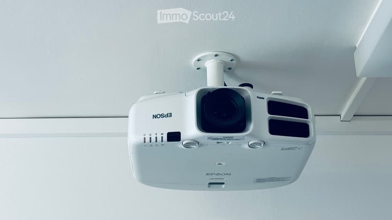 A white Epson projector mounted on the ceiling, with visible control buttons and lens.