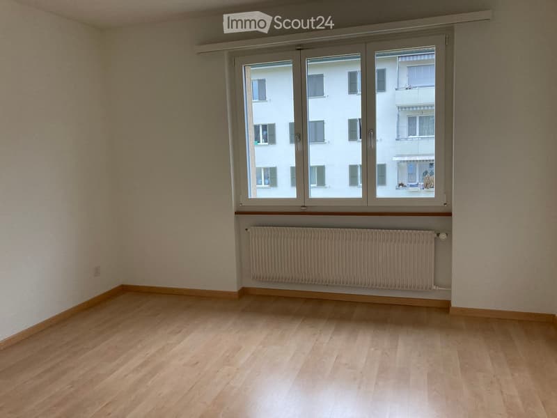 Empty room with wooden floor, large window, white walls, radiator, white building outside