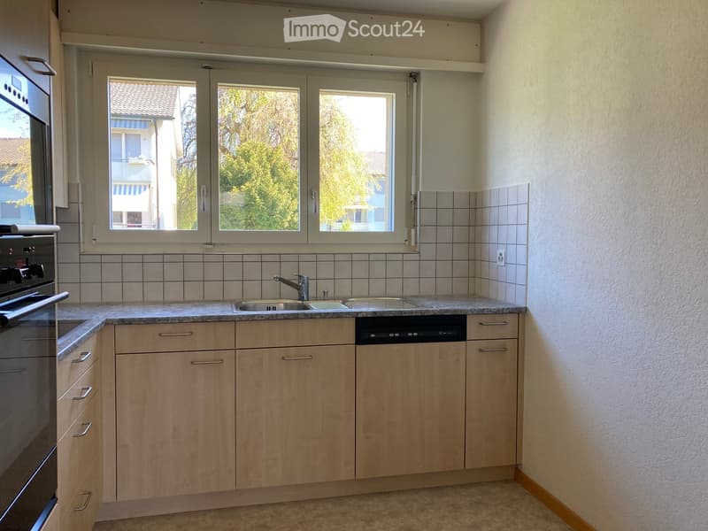 Modern kitchen with light wooden cabinets, granite countertop, sink, faucet, dishwasher, and oven.