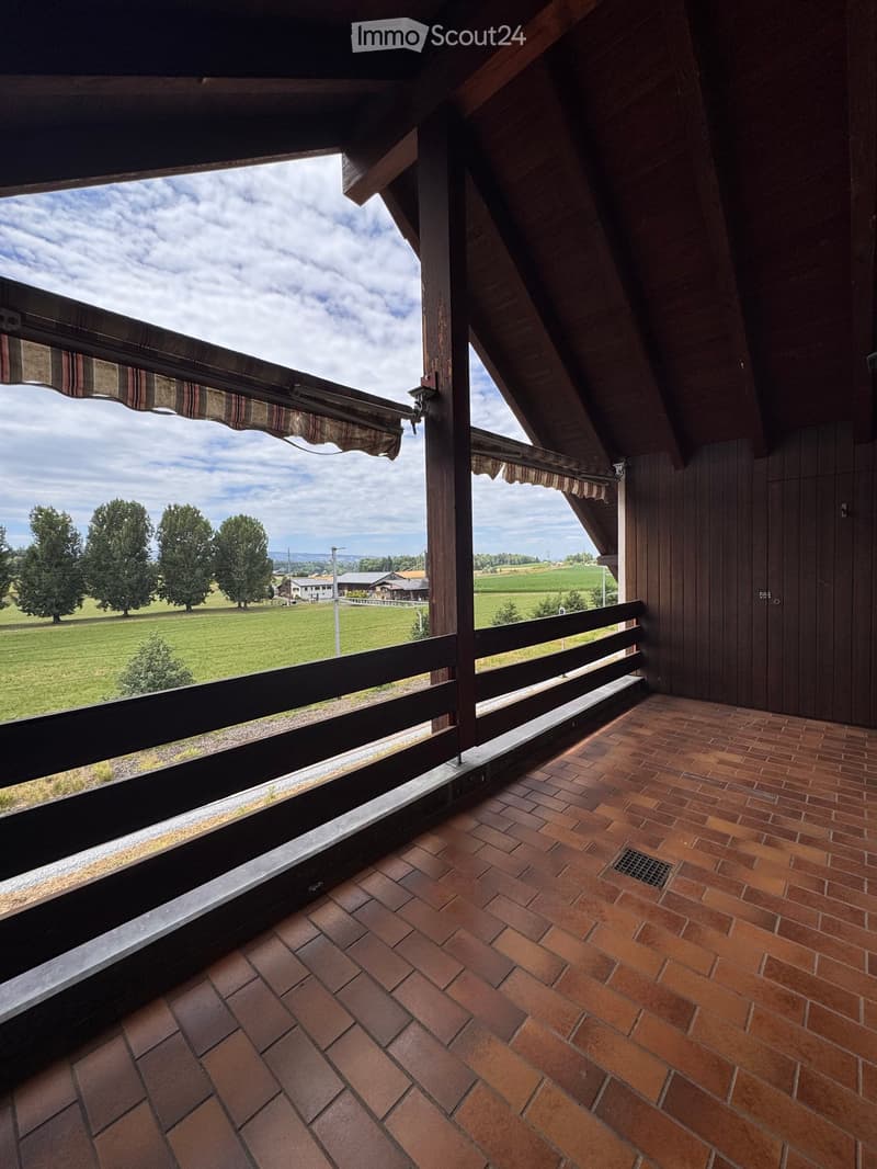 Balcony with brick tiles, wooden railing, and scenic countryside view.