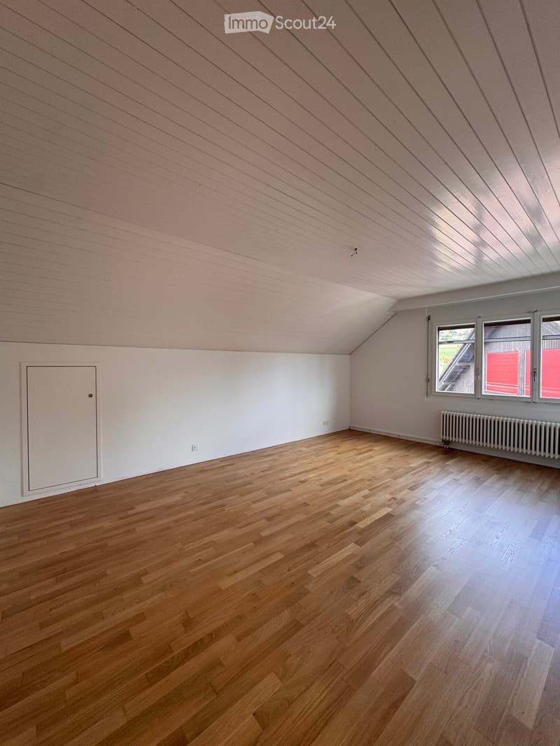 Empty attic room with wooden flooring, white walls, and large windows. No furniture or equipment present.