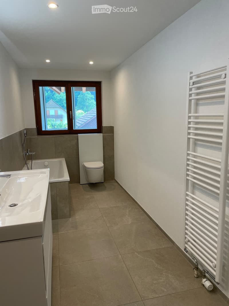 Modern bathroom with a large window, white sink, bathtub, toilet, and a white radiator on the wall.