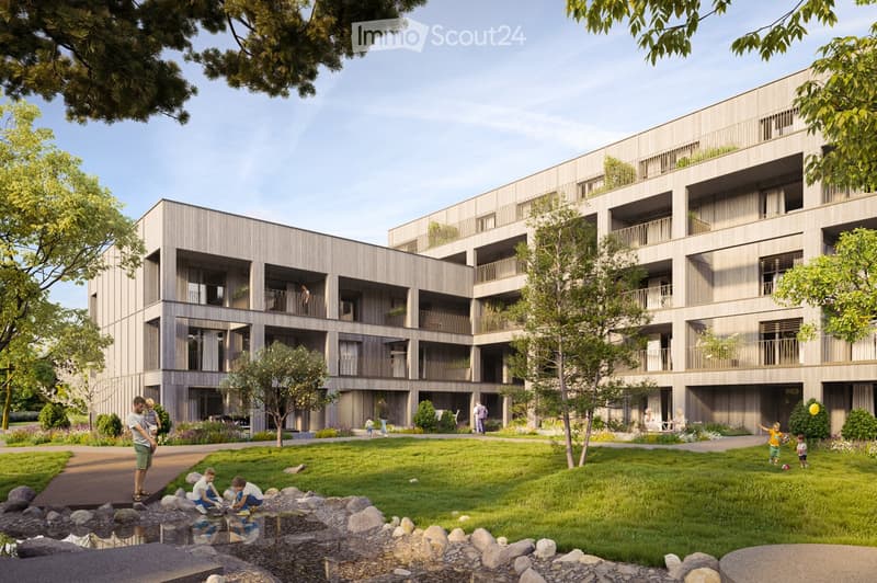 Modern multi-story residential building with balconies and greenery, surrounded by a landscaped garden area with children playing and a small water feature.