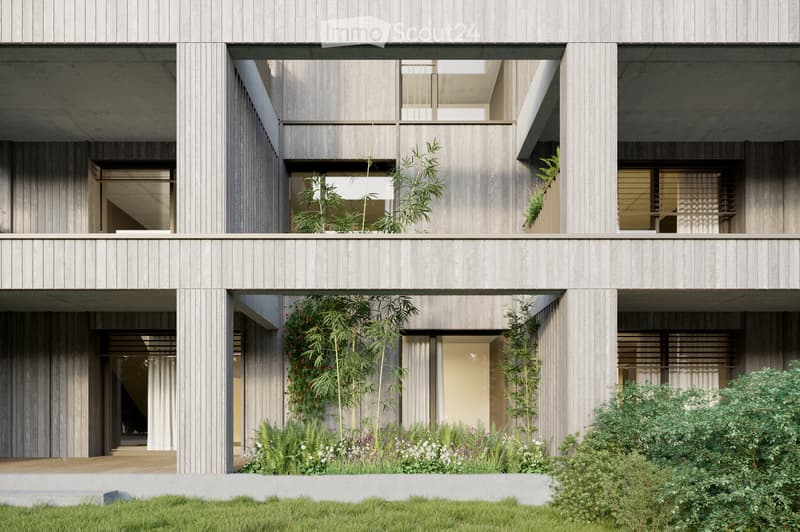 Modern two-story building with a raised ground floor, wooden facade, and greenery integrated into the design. Features include a covered entrance, large windows, and a balcony area on the upper level.