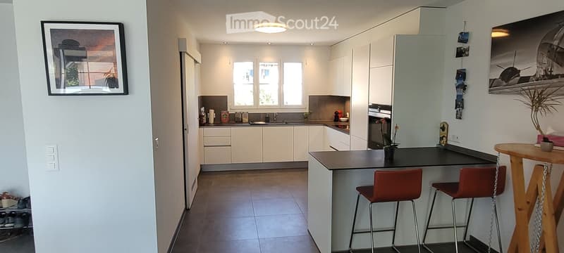 Modern kitchen with white cabinetry, stainless steel appliances, a central island with bar stools, and a small dining area with a round table and chairs.