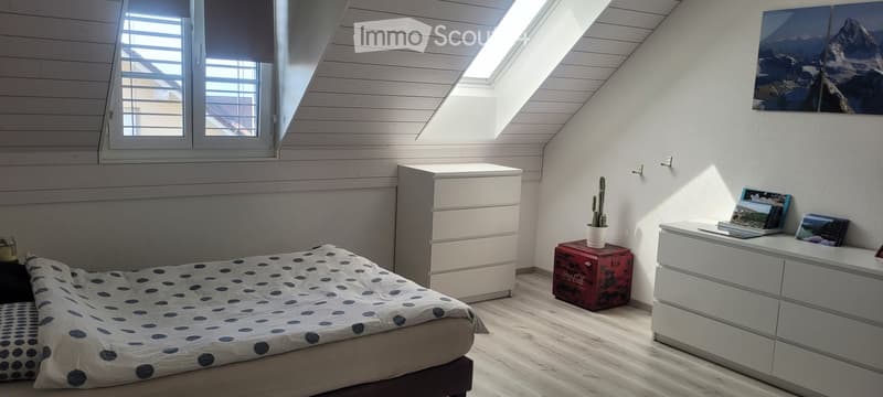 Cozy attic bedroom with slanted wooden ceiling, skylight windows, bed with polka dot bedding, nightstand, drawer unit, laptop, cactus, and picture frames on a white dresser.