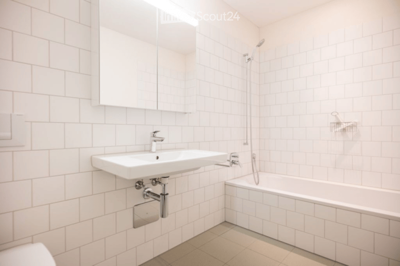 Modern bathroom with white tiled walls and floor, featuring a sink, bathtub, mirror, and showerhead.