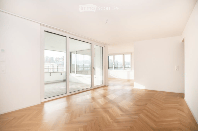 Empty room with wooden flooring, large glass sliding doors leading to a balcony, and white walls.