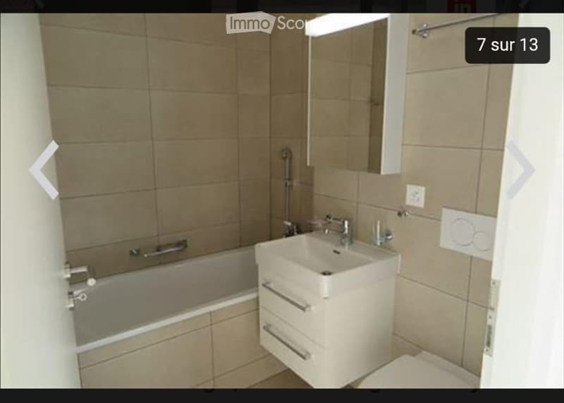 Modern bathroom with a bathtub, sink, mirror, and cabinet. Beige tiled walls and floor.