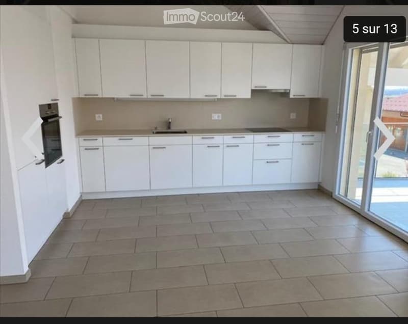 Modern kitchen with white cabinets, tiled floor, and built-in oven. Features a sink and faucet, with large windows providing natural light.