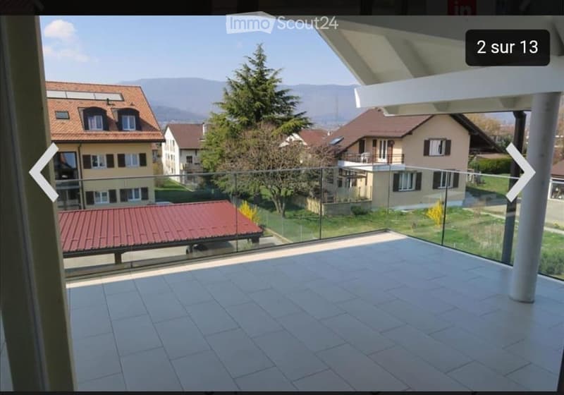 Balcony with tiled floor, glass railing, overlooking a residential area with houses and trees.