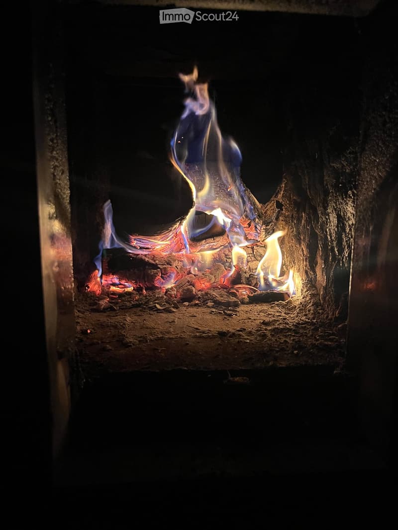 A fireplace with active flames and burning wood, surrounded by dark stone or brick walls.