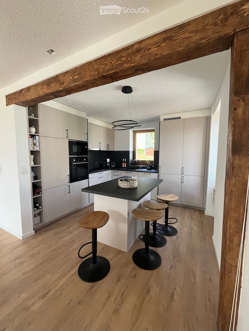 Modern kitchen with white cabinets, black countertop, wooden stools, and a hanging pendant light.
