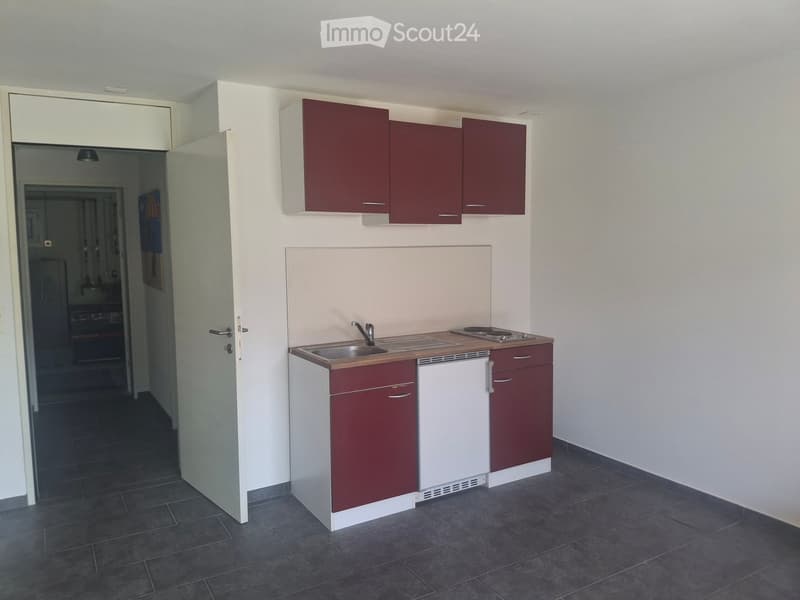 Compact kitchen with red and white cabinets, a sink, a small stove, and a countertop.
