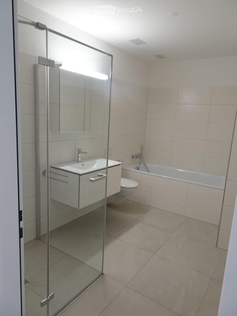 Modern bathroom with a white tiled floor and walls, featuring a sink with a faucet, a bathtub, a toilet, and a glass-enclosed shower stall.