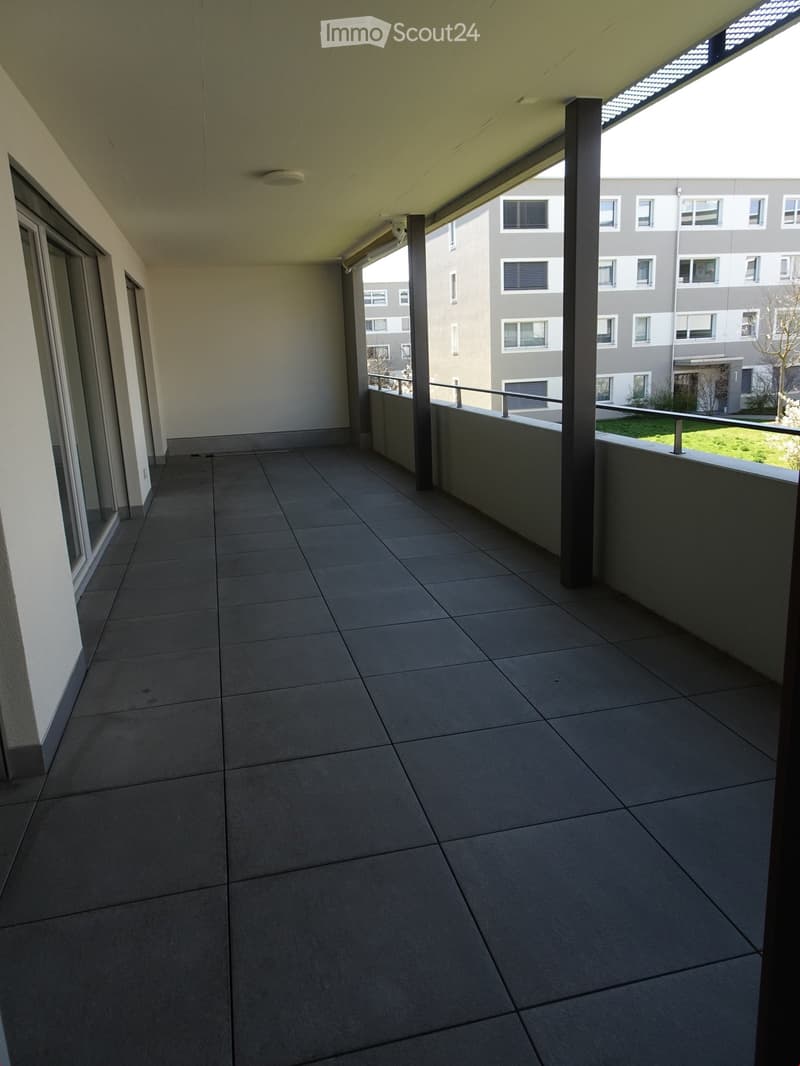 Empty balcony with tiled floor, metal railing, and a view of a modern apartment building.