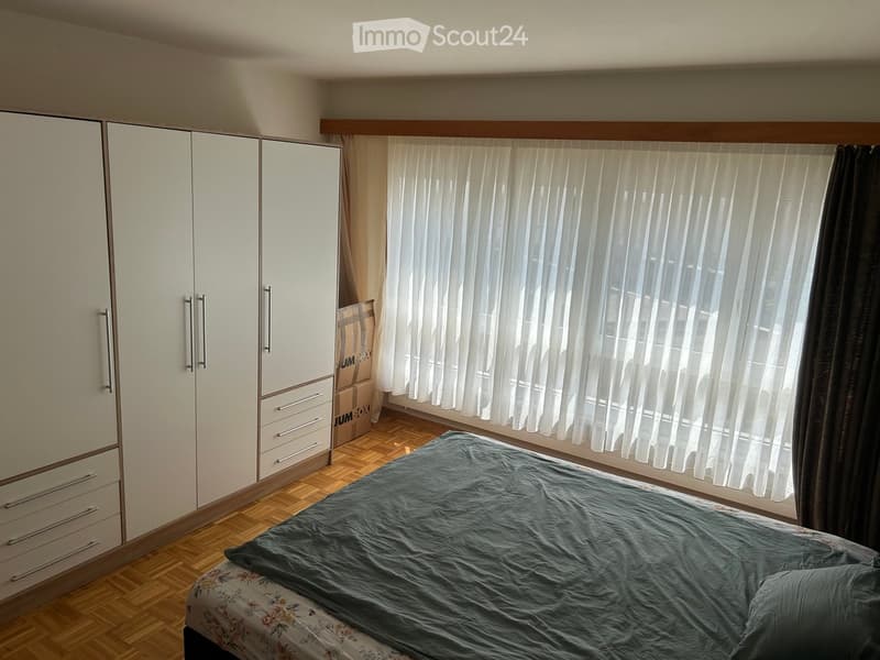 Bedroom with a large bed, white wardrobe, and large window with white blinds.