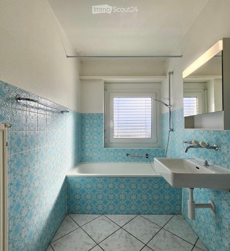 Bathroom with blue tiled walls and floor, a bathtub, a sink with a mirror, and a window with blinds.