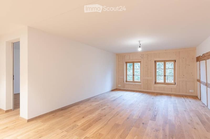 Empty room with wooden flooring, white walls, and two windows with wooden frames. No furniture or equipment present.
