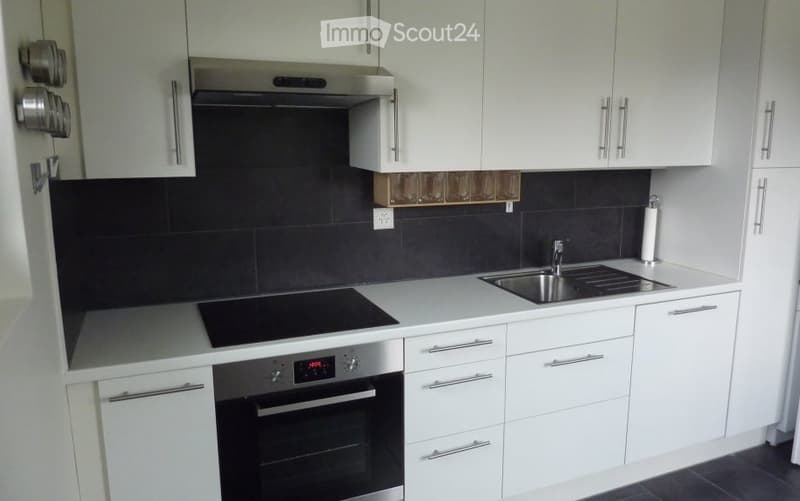 Modern kitchen with white cabinets, stainless steel appliances, black tiled backsplash, and a built-in oven and stove.