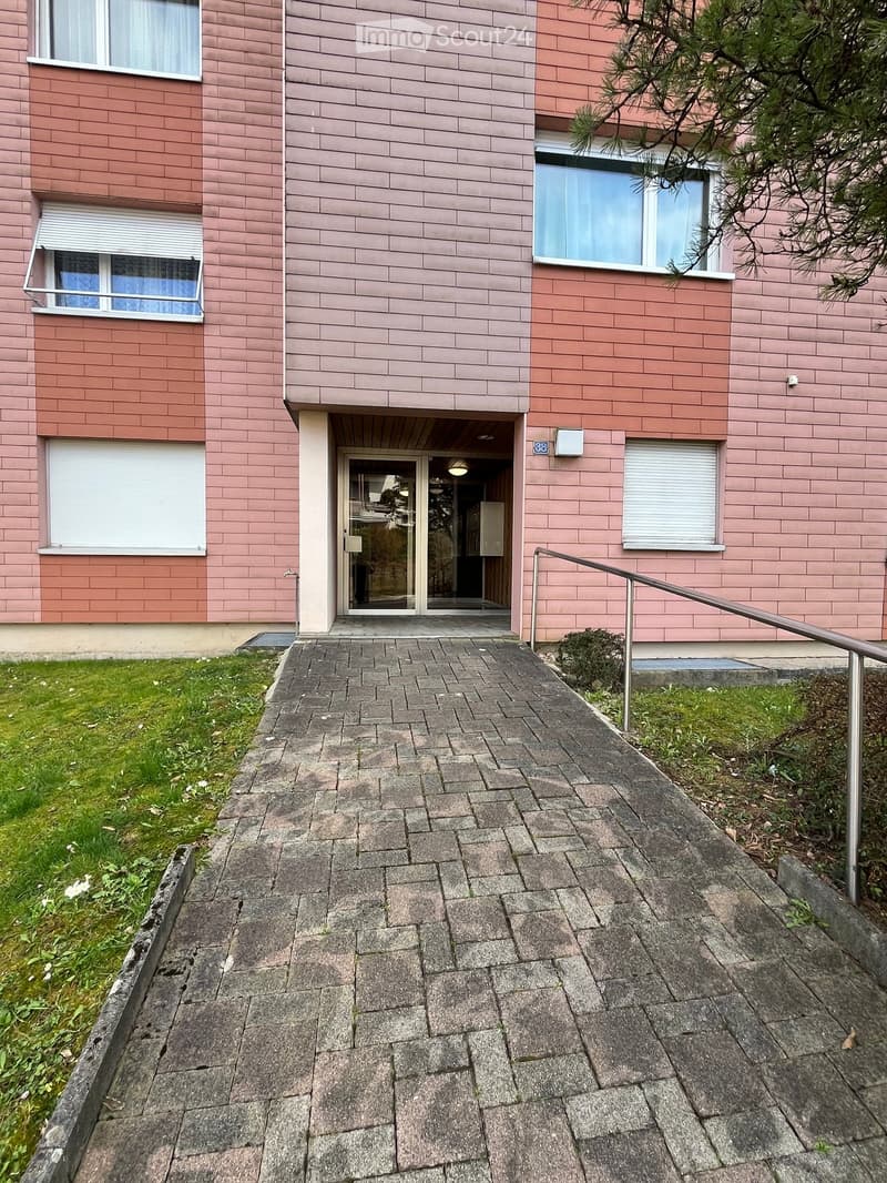 Exterior view of a multi-story building with pink brick facade, windows, and a paved entrance pathway.