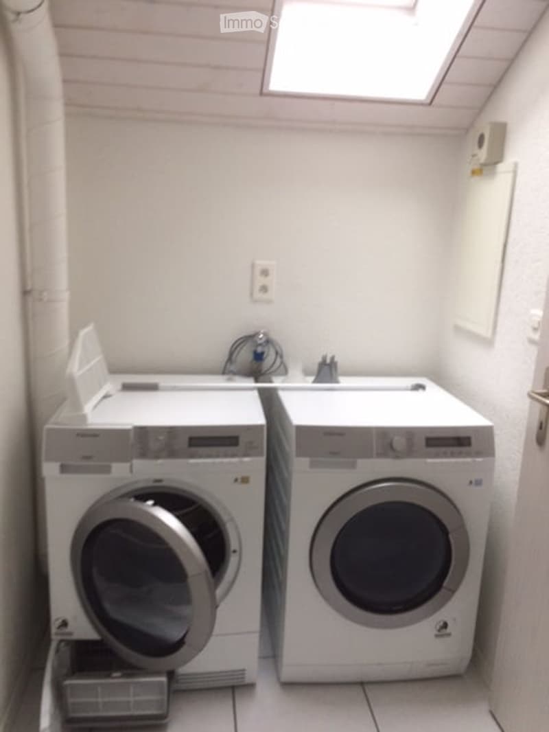 Small bathroom with a washing machine and dryer, white tiled floor, and a skylight window above.