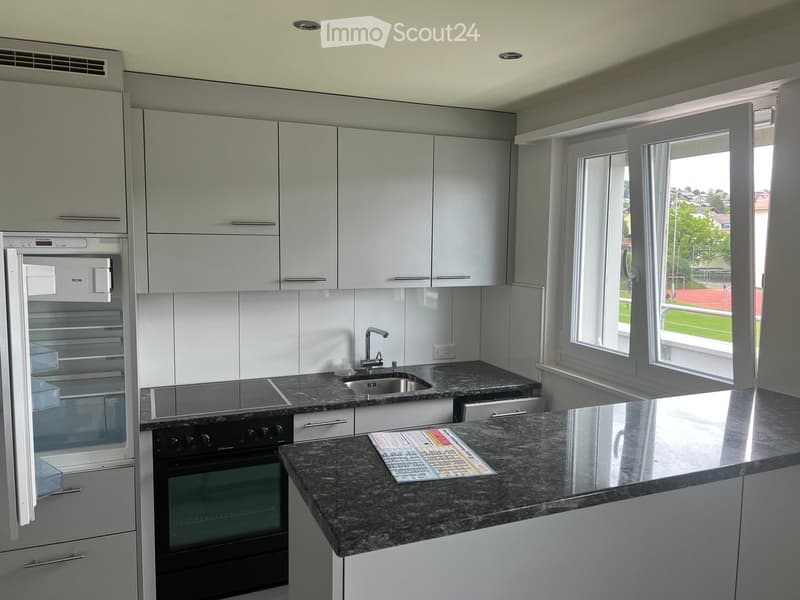 Modern kitchen with white cabinets, granite countertop, stainless steel appliances, and large windows overlooking a sports field.