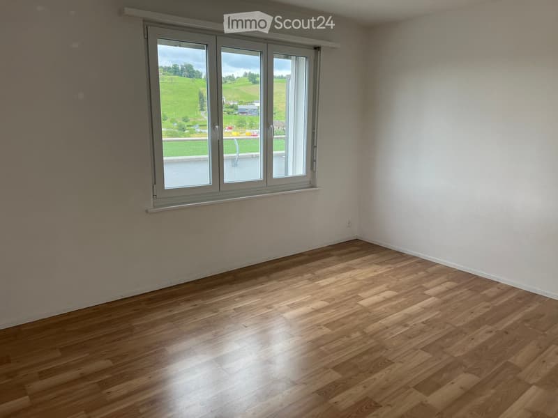 Empty room with wooden flooring and large window showing a green landscape view.