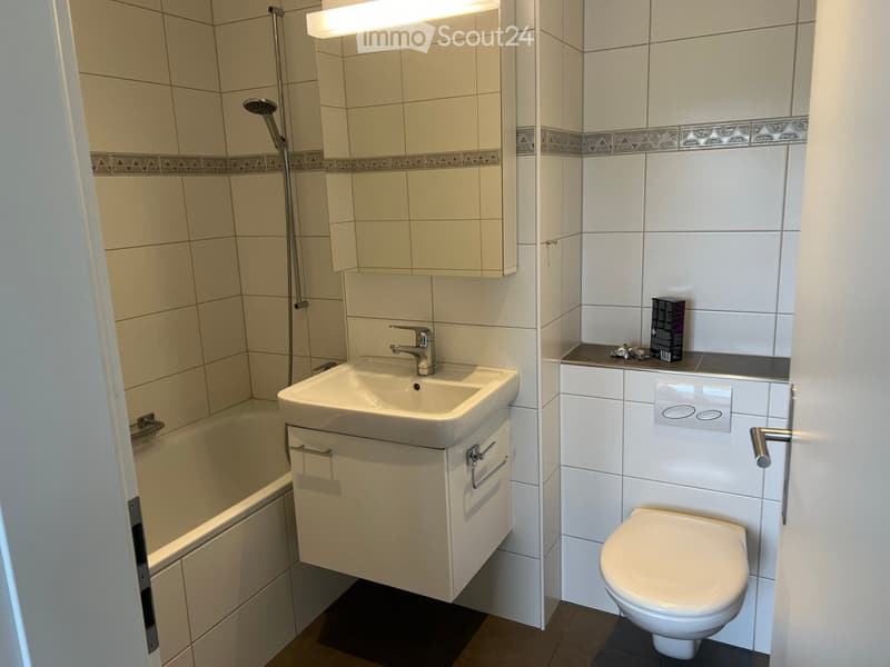 Modern bathroom with a bathtub, sink, toilet, and showerhead. Features white tiles, a decorative border, and a built-in cabinet under the sink.