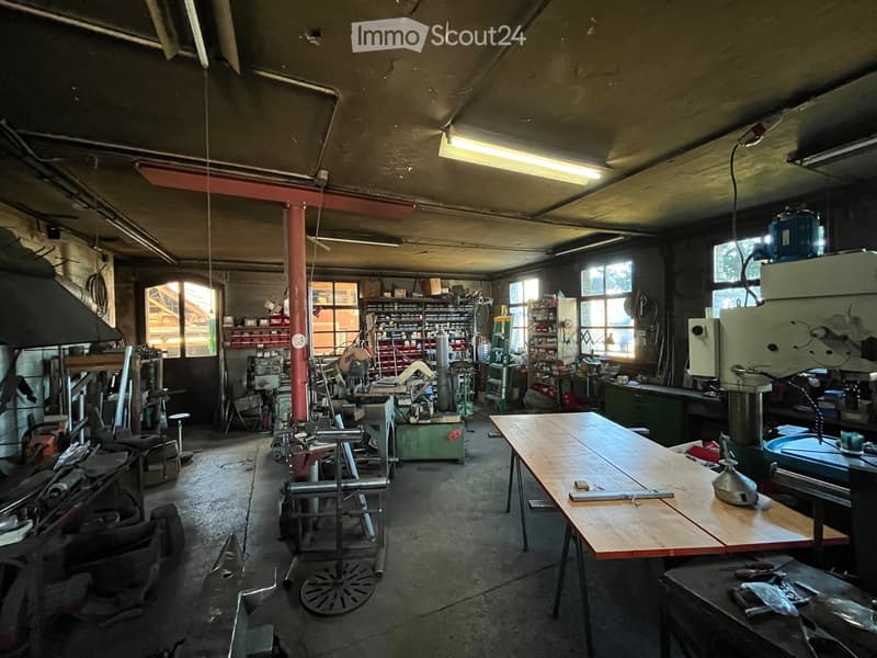 A spacious workshop with a large wooden workbench, various tools, machinery, and shelves filled with supplies.