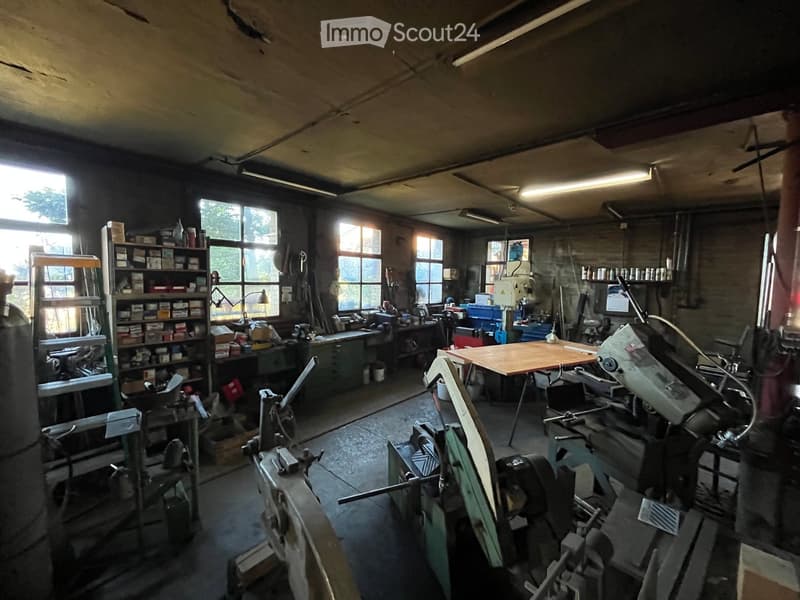 Workshop with large windows, wooden table, shelves filled with tools and supplies, various machinery and equipment.
