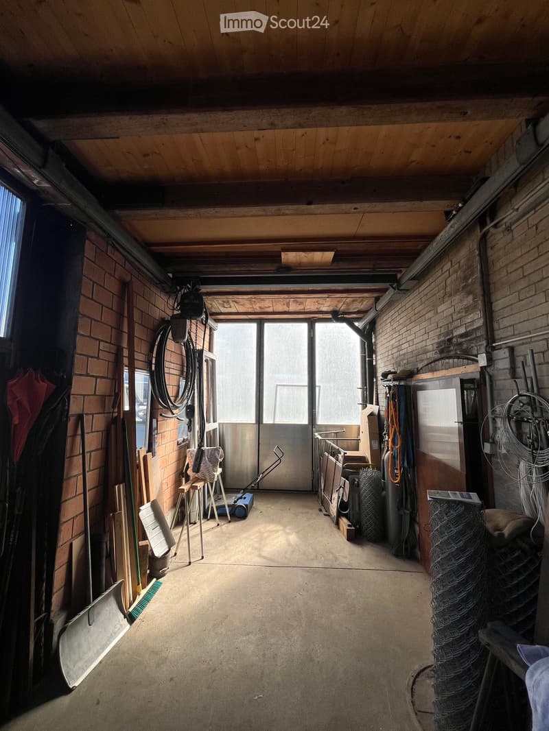 Empty garage with concrete floor, brick walls, large overhead door, and scattered tools and storage items along the walls.