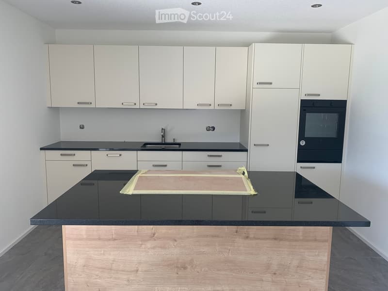 Modern kitchen with white cabinets, black countertops, and a central island with wooden base.