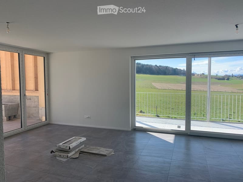 Empty room with tiled floor, large sliding glass doors leading to a balcony with a scenic view, and some stacked boxes on the floor.