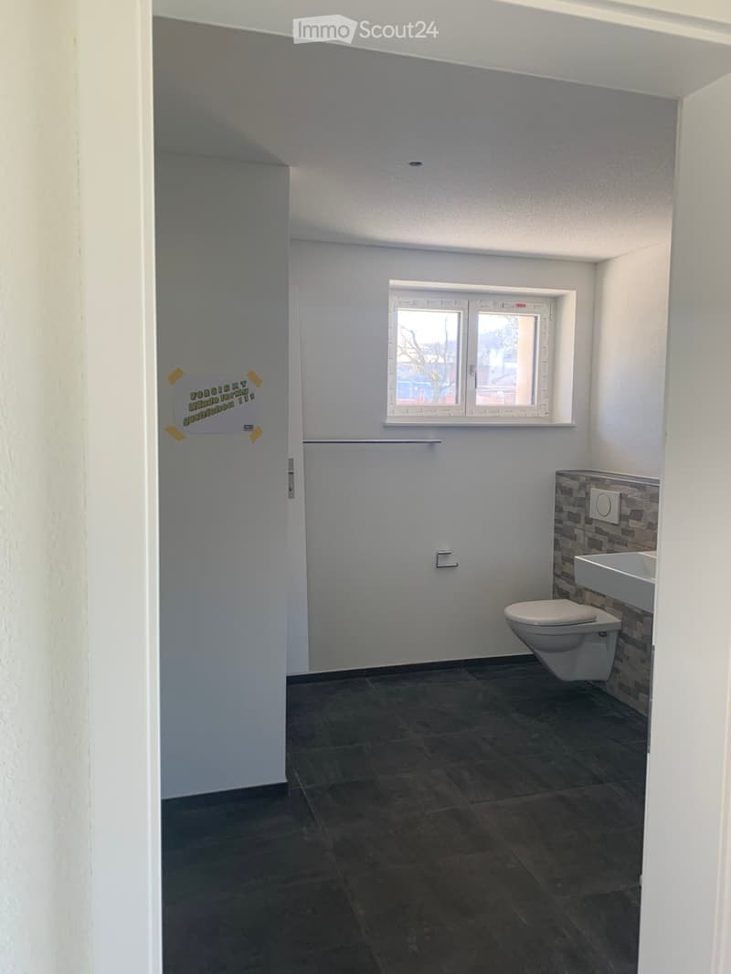 Small bathroom with dark tiled floor, white walls, a toilet, a sink, and a window above the sink.