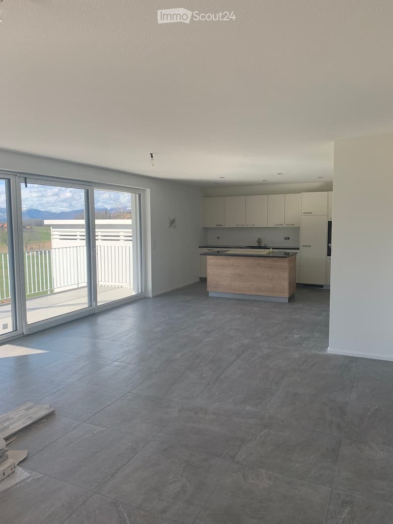 Modern kitchen with grey tiled floor, white cabinets, and a wooden kitchen island. Large sliding glass doors lead to a balcony with a scenic mountain view.