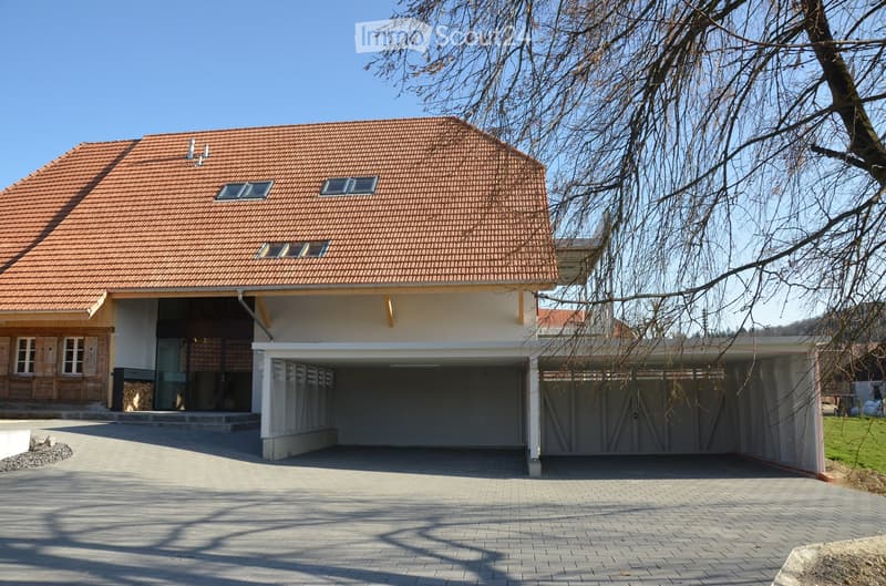 Two-story house with a red-tiled roof, white walls, and a large attached garage. The house features multiple windows and a modern design with a paved driveway.