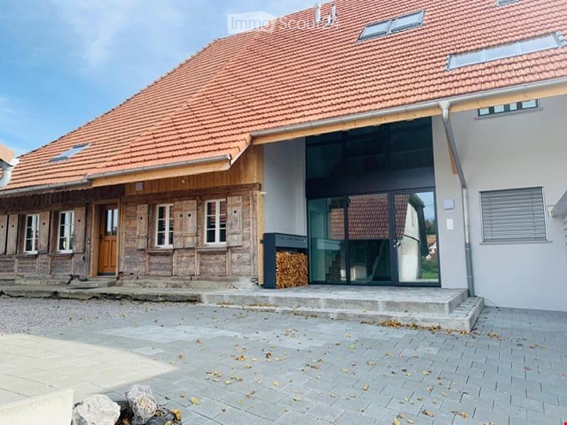 Two-story house with a red-tiled roof, stone and wooden facade, large glass entrance, and a paved driveway.