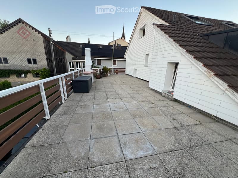 Balcony with concrete tiles, wooden railing, small storage box, and potted plants.