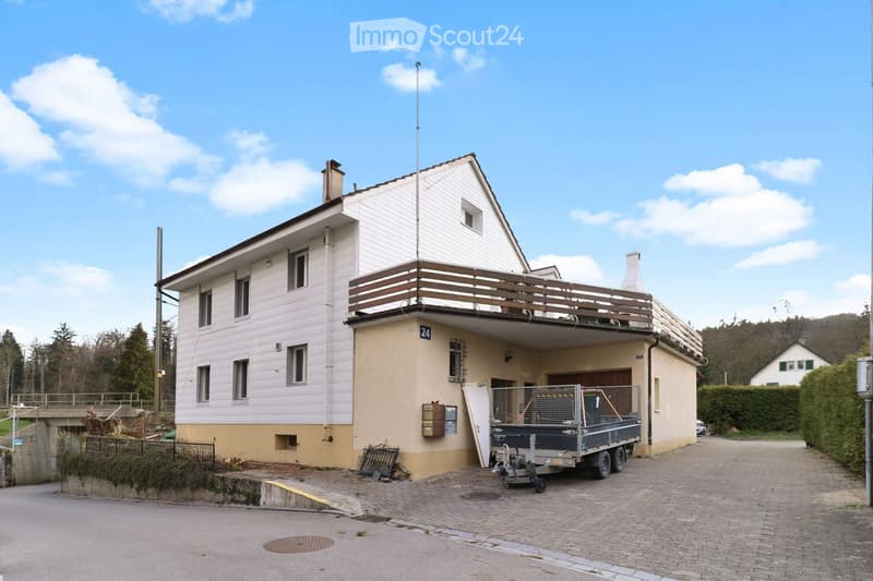Two-story house with white siding, balcony on the upper level, garage, and trailer parked in front.