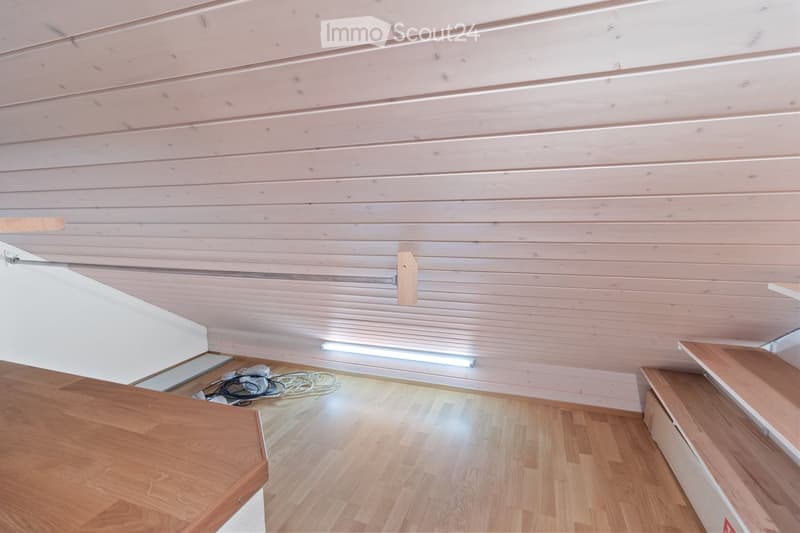 Empty room with wooden flooring and paneled walls, featuring built-in wooden shelves and a small wooden table.