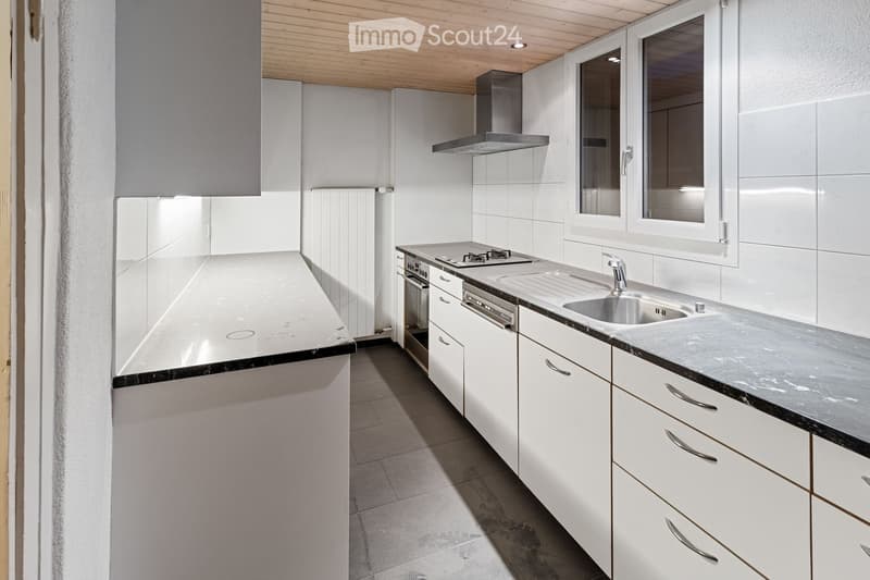 Modern kitchen with white cabinets, stainless steel appliances, and a black countertop. Features include a sink, faucet, oven, dishwasher, and a range hood.