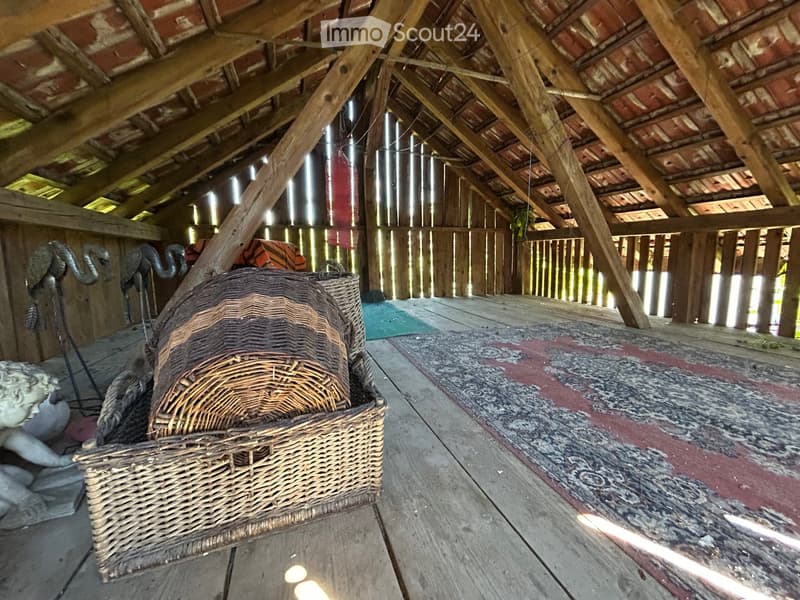 Wooden attic space with exposed beams, a large wicker basket, a statue, and a colorful rug on the floor.
