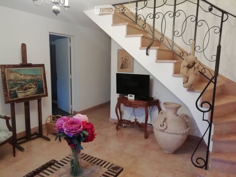 A well-lit hallway with a staircase, a small wooden table with a TV, a large ceramic vase, a painting on an easel, and a flower arrangement in a vase on the floor.