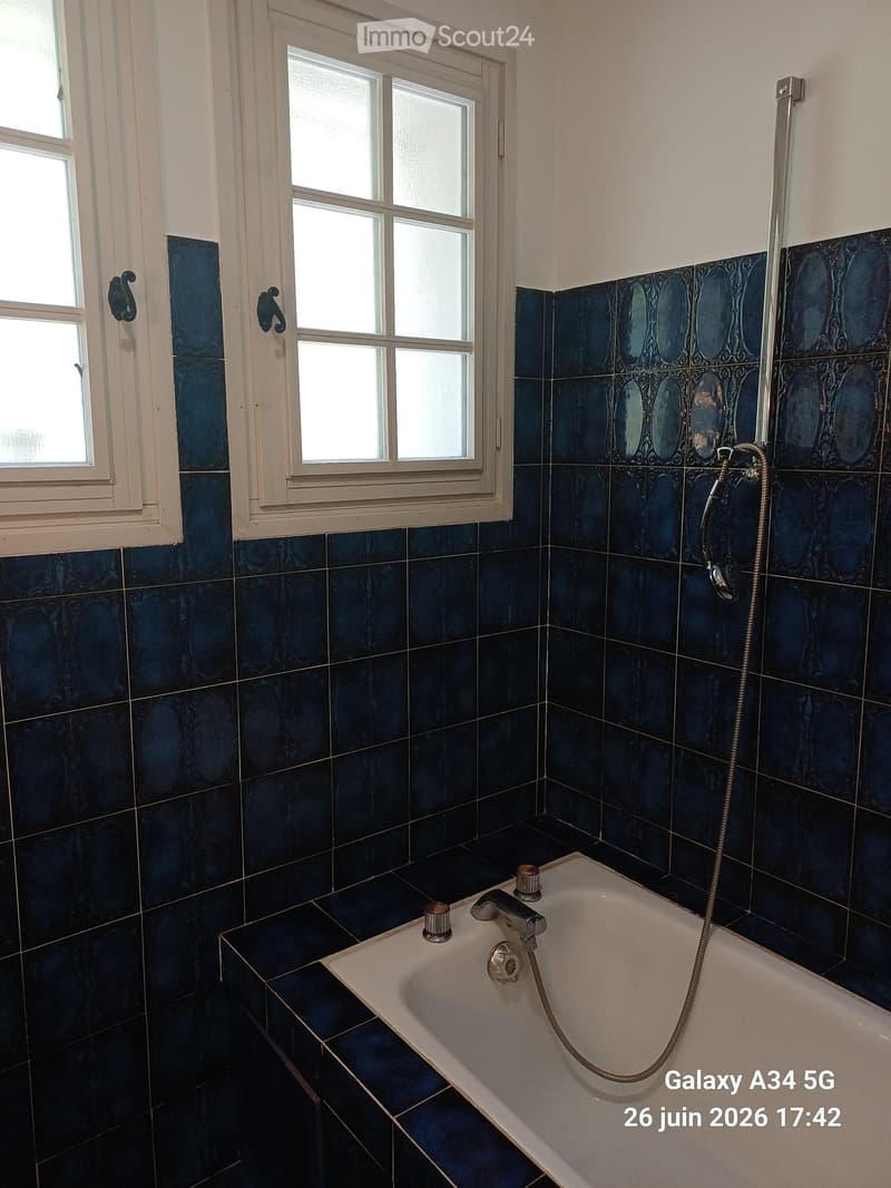 Bathroom with dark blue tiles, a white bathtub, and a showerhead attached to the wall.