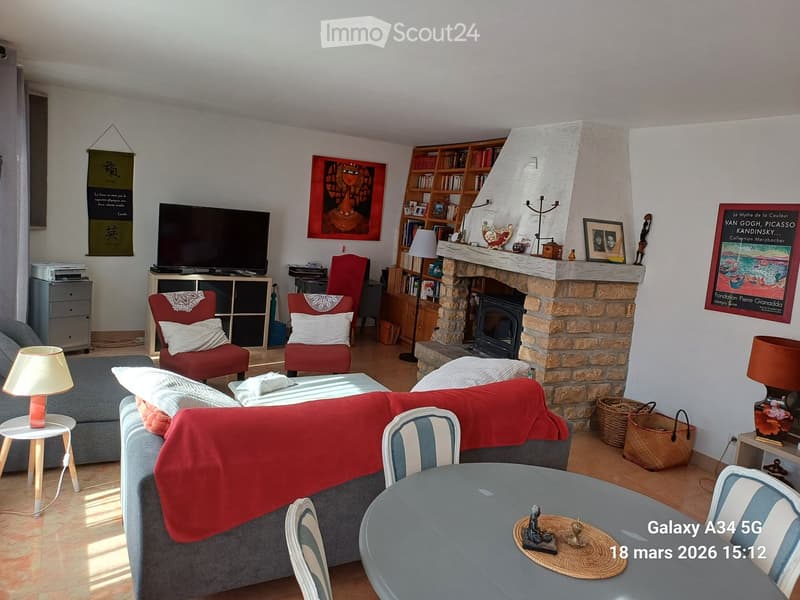 Cozy living room with a grey sofa, red throw, coffee table, armchairs, bookshelf, television, and a stone fireplace.
